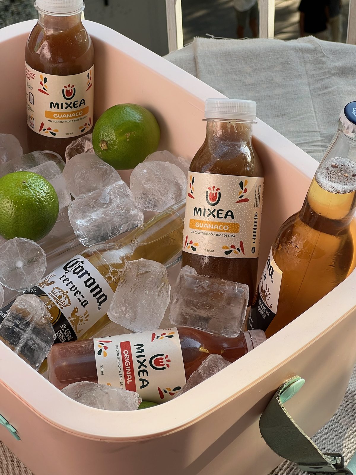Botellas de Mixea en hielera con hielo, limas y cervezas